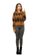 A full-length shot of a Teenager girl with brown sweater pointing with the index finger a great idea over isolated white background