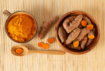 Turmeric roots and powder in bowls on bamboo background. Top view