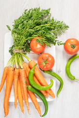 Fresh carrots with green leaves? green peppers and tomatoes on light gray wooden background. Vertical image