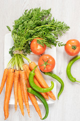 Obraz na płótnie Canvas Fresh carrots with green leaves? green peppers and tomatoes on light gray wooden background. Vertical image