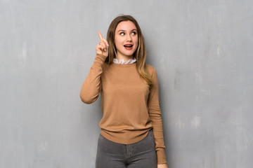Teenager girl over textured wall intending to realizes the solution while lifting a finger up