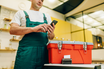 Repairman in uniform holds phone against toolbox