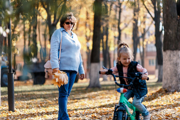 A cute little girl riding a bike with her granny in autumn