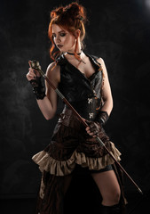 A beautiful red-haired cosplayer girl wearing a Victorian-style steampunk costume with a big breast in a deep neckline thoughtfully holds a cane in her hands on a dark background.