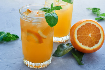 two glasses of fresh orange juice with orange slices, ice, mint leaves on a gray background