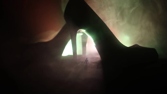 Artwork decoration. Silhouette of a man standing in the middle of the road on a misty night with giant high heel women shoes. Women power or women domination concept. Selective focus