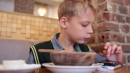 Cute young kid playing computer video games while eating food at restaurant. Real time full hd video footage.