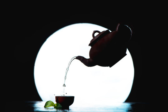 Flying Tea Pot Silhouette Against A Full Moon Silhouette. Asian Tea Ceremony Pouring Tea With Copy Space