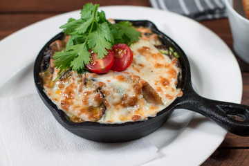 Grilled eggplant stuffed with tomatoes, nuts, pomegranate and herbs and cheese, baked in a black pan. Wood background