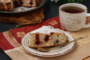 Berry pie with cherries is located on a plate on a dark background