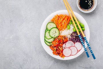 Salmon poke bowl with rice, radish,cucumber, carrots, edamame, red cabbage and sesame seeds.