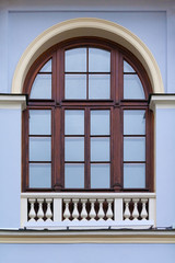 Close up view on a arched window with wooden frame and decorative white fence on bottom on a  facade of blue ancient building