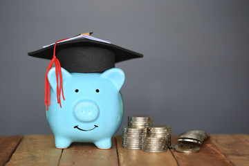Graduation hat on blue piggy bank with stack of coins money on black background, Saving money for...