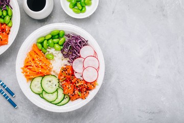 Salmon poke bowl with rice, radish,cucumber, carrots, edamame, red cabbage and sesame seeds.
