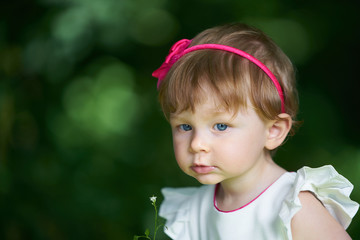 Portrait of a one-year-old girl with blue eyes and hair decoration looking aside