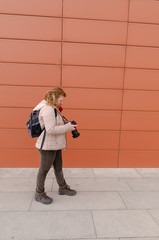 Blond caucasian woman is walking outdoors and  she is checking  her camera.