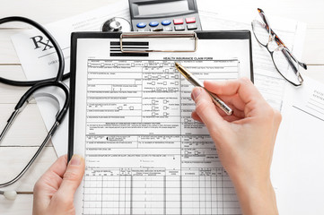 Woman filling health insurance claim form on clipboard.