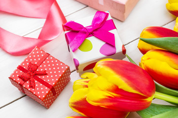 Fresh beautiful tulips with gift boxes on white wooden background.
