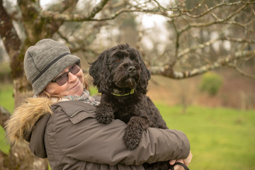 Woman carrying black cockapoo outdoors 