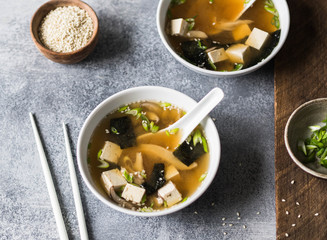 Japanese miso soup with mushrooms in a white bowls with a spoon and white chopsticks on a grey and...