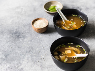 Japanese miso soup with oyster mushrooms in a black bowls with a spoon on a grey background