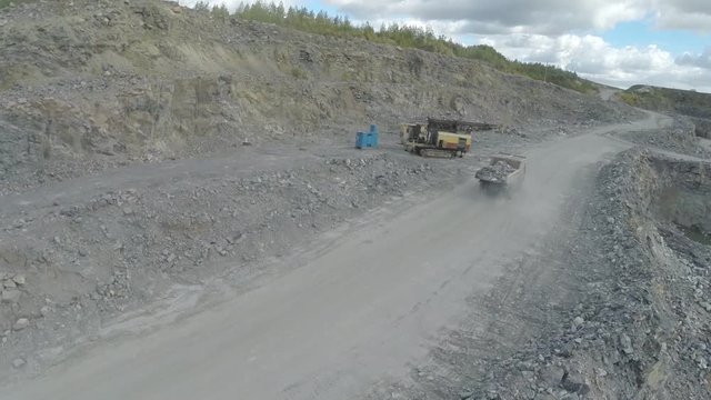 Aerial view of opencast mining quarry with lots of machinery at work - view from above. Loaded rock dump truck rides along the road, close-up.
