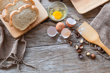 Sliced bread placing on wooden plate on the wooden table and spoon. Ingredients are all around such as flour, eggs and macadamia nuts.