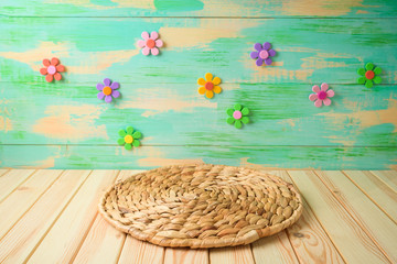 Empty wooden table with round wicker placemat over colorful background.