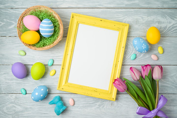 Easter holiday background with easter eggs in basket, photo frame and tulip flowers on wooden table.