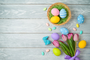 Fototapeta premium Easter holiday background with easter eggs in basket and tulip flowers on wooden table.