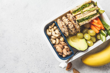 School healthy lunch box with sandwich, cookies, fruits and avocado on white background.