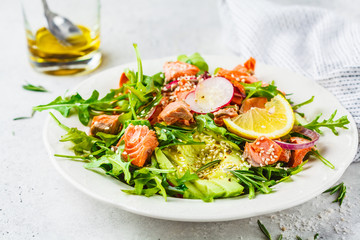 Baked red fish salad with avocado, cucumber, radish and arugula in white plate.