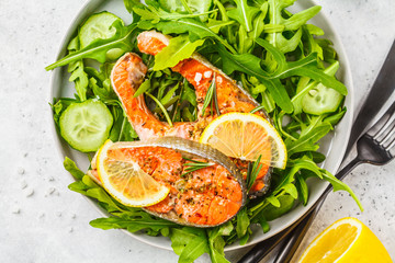 Fried red fish with arugula and cucumber salad in white plate.