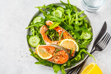 Fried red fish with arugula and cucumber salad in white plate, copy space.