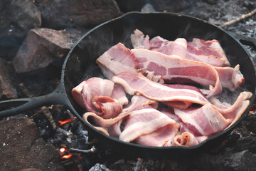 Bacon cooking in cast iron over campfire 