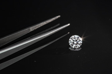 1.00 carat size diamond compared with tweezers on black reflection background