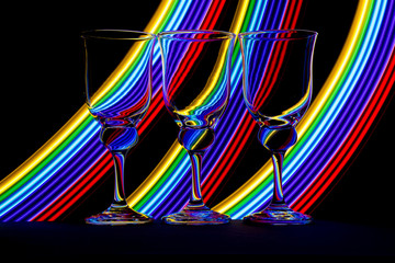 Wine glasses in a row isolated against a black background with colorful streaks of neon light painting behind them