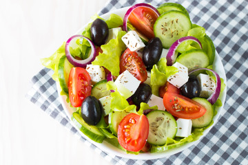 Fresh Greek salad made of cherry tomato, ruccola, arugula, feta, olives, cucumbers, onion and spices. Caesar salad in a white bowl on wooden background. Healthy organic diet food concept.