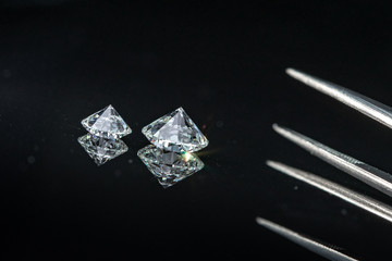 1.00 carat size and 2.50 carat size bottom up diamonds with tweezers on black background