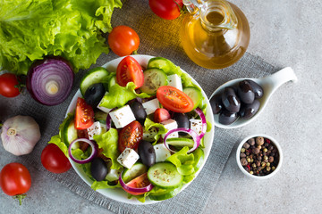 Fresh Greek salad made of cherry tomato, ruccola, arugula, feta, olives, cucumbers, onion and spices. Caesar salad in a white bowl on wooden background. Healthy organic diet food concept.