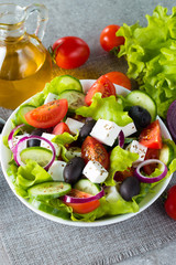 Fresh Greek salad made of cherry tomato, ruccola, arugula, feta, olives, cucumbers, onion and spices. Caesar salad in a white bowl on wooden background. Healthy organic diet food concept.