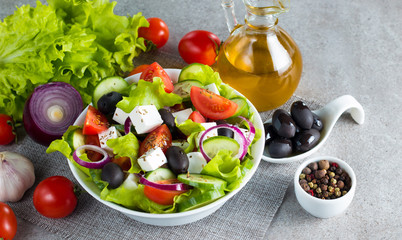Fresh Greek salad made of cherry tomato, ruccola, arugula, feta, olives, cucumbers, onion and spices. Caesar salad in a white bowl on wooden background. Healthy organic diet food concept.