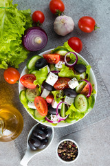 Fresh Greek salad made of cherry tomato, ruccola, arugula, feta, olives, cucumbers, onion and spices. Caesar salad in a white bowl on wooden background. Healthy organic diet food concept.