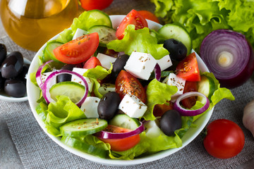 Fresh Greek salad made of cherry tomato, ruccola, arugula, feta, olives, cucumbers, onion and spices. Caesar salad in a white bowl on wooden background. Healthy organic diet food concept.