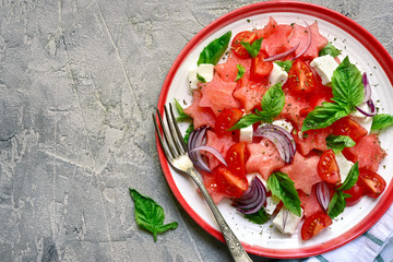 Watermelon salad with tomato, feta cheese, red onion and basil on a plate.Top view with copy space.