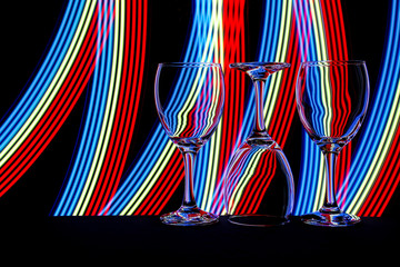 Wine glasses in a row isolated against a black background with colorful streaks of neon light painting behind them