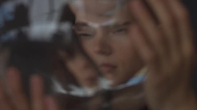 Close up portrait of female face through wavering glass macro detail 4k. Attractive woman posing looking through jar indoors studio photoshoot. Youth beauty concept self-care product teen problems