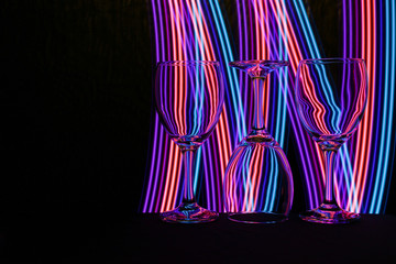 Wine glasses in a row isolated against a black background with colorful streaks of neon light painting behind them