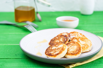 Homemade cottage cheese pancakes with honey on a plate on a wooden table