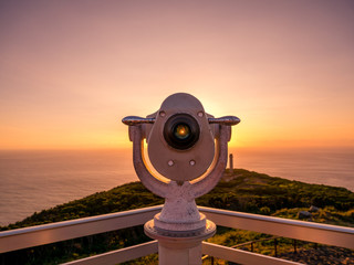 Image of viewpoint with binoculars during colorful sunset pointing at the ocean - obrazy, fototapety, plakaty